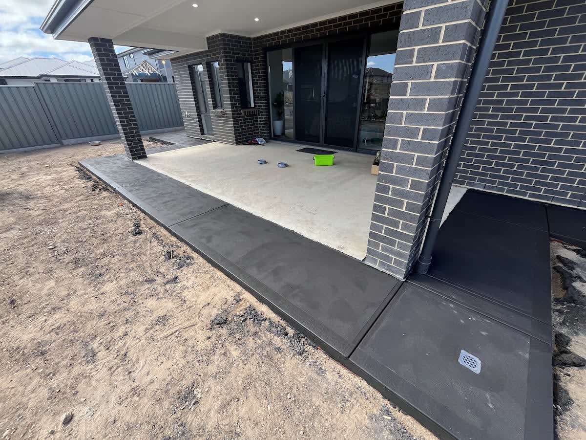 A charcoal exposed-aggregate and broom-finish patio slab against a modern dark-brick home