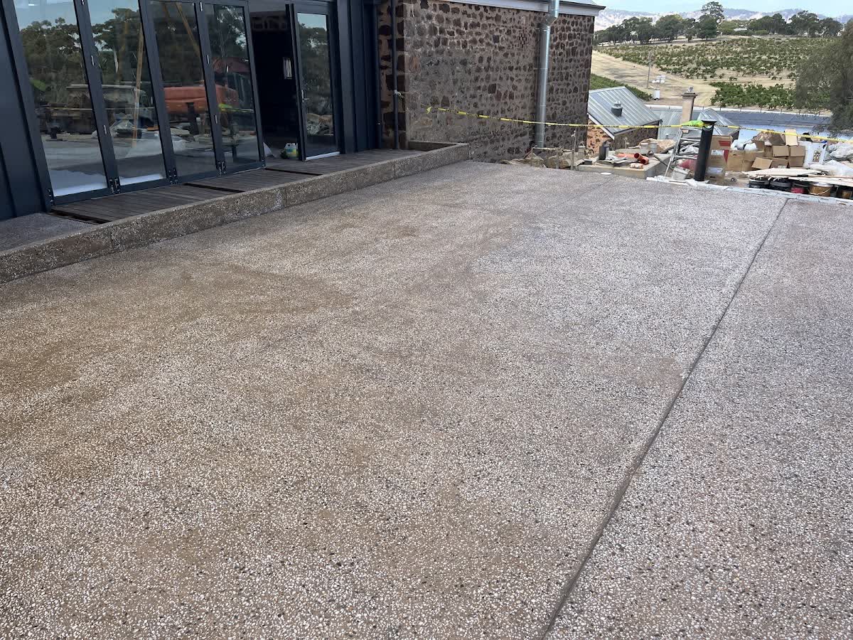 An exposed-aggregate patio poured beside the bifold doors of a stone country home